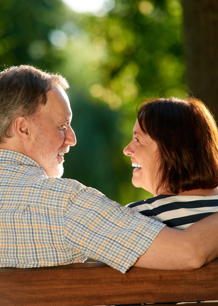 A smiling older couple sitting on a bench.